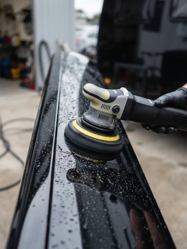 Macro close-up of a dual-action polisher refining a deep black caravan gelcoat, high-contrast reflections, water beading, professional detailing setup, overcast daylight, 35mm