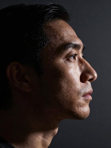 A striking chiaroscuro studio portrait of a subject in profile, dramatic low-key lighting casting deep shadows, sharp rim light highlighting the jawline, dark slate background.