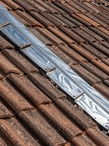 Gros plan sur des tuiles plates traditionnelles parfaitement alignées sur un toit en pente, avec un raccord en zinc brillant sous une lumière de Seine-et-Marne.