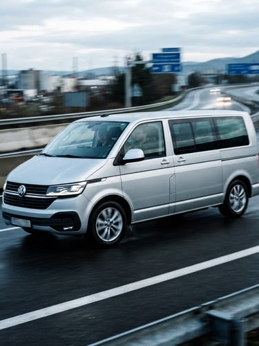 Dynamic low-angle tracking shot of a modern silver express minivan speeding on a European highway in cool morning daylight, motion blur, sharp high-contrast industrial tones, 35mm