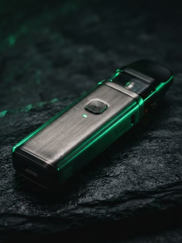 Macro close-up of a premium brushed-metal vape device on a dark slate surface, dramatic emerald green rim lighting, high-contrast, 35mm photography