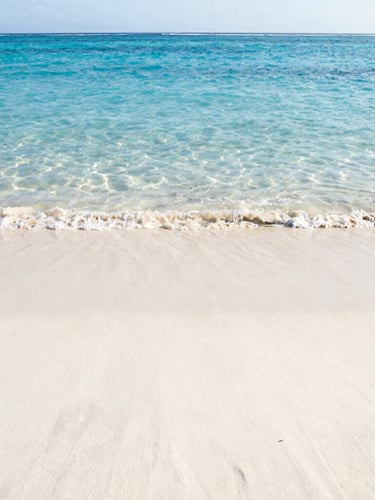 Pristine empty tropical beach with soft white sand and crystal clear ocean water, low horizon, wide environmental shot, golden-hour sunlight, peaceful and silent