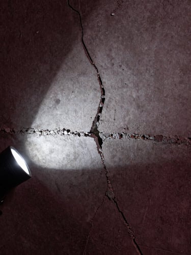 Macro shot of a structural crack in raw concrete, highlighted by a sharp, cool-toned flashlight beam, industrial engineering photography, high-contrast, deep charcoal and burgundy tones.