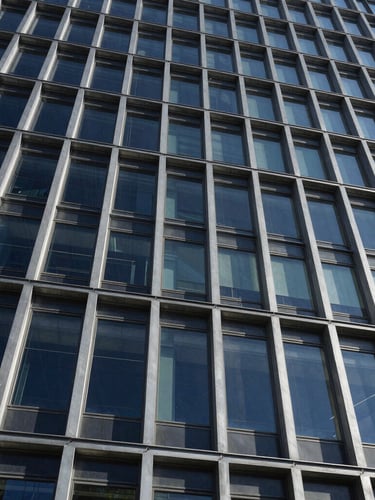Low-angle architectural photograph of a completed glass and steel building facade, sharp shadows, high-contrast daylight, emphasizing structural joints and clean lines, wide-angle perspective.