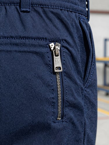 Macro close-up shot of a triple-stitched seam on heavy-duty navy canvas work trousers, silver YKK zipper detail, high depth of field, sharp industrial focus