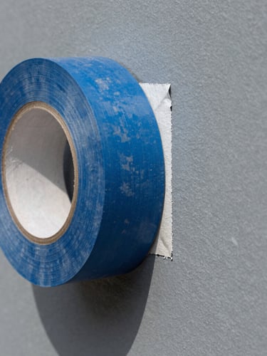 Macro shot of sharp blue painter tape being peeled back to reveal a razor-sharp, crisp paint line on a slate gray wall, bright natural daylight.