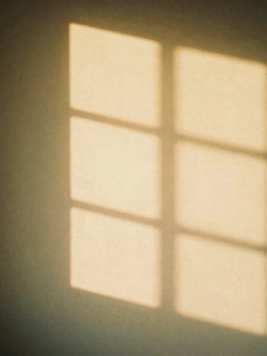 Soft diffused golden hour light shining through a window casting gentle shadows on a warm plaster wall, minimalist aesthetic, warm editorial photography, 35mm film