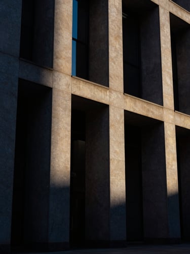 Portrait-oriented, high-contrast, dramatic architectural shot of a modern courthouse facade with sharp angles, strong directional light, deep shadows, and rich dark tones, 35mm.