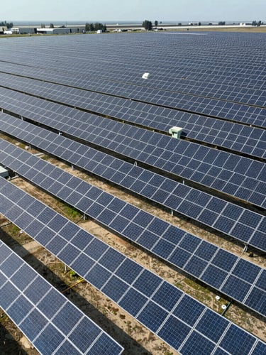 Wide-angle aerial drone shot of a massive utility-scale solar farm stretching to the horizon, bright daylight, sharp shadows on rows of photovoltaic panels, 35mm.