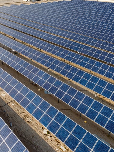 Wide-angle aerial drone shot of Al Dhafra solar farm, thousands of high-contrast blue solar panels stretching in perfect geometric rows under crisp morning sun, 35mm.