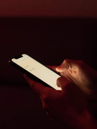 Close-up of hands holding a smartphone with a warm screen glow in a dark room, moody low-key lighting, deep burgundy shadows, 35mm film grain