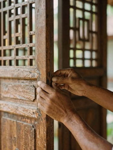 Vertical portrait of a craftsman's hands gently inspecting a joint in a weathered teak screen, warm soft morning sunlight, shallow depth of field, Bali villa background
