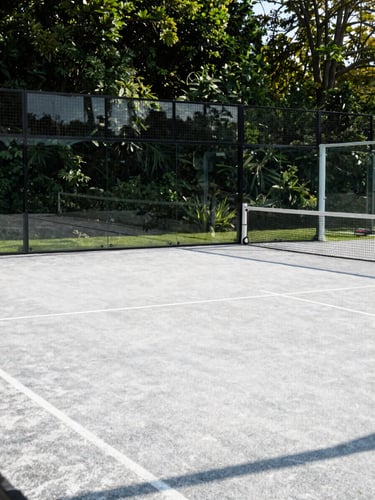 Bright morning light casting sharp shadows across a pristine outdoor padel court with forest green surroundings, Somerset, 35mm photography