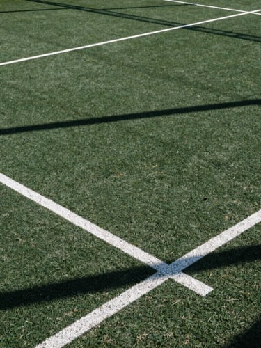 Dynamic low-angle shot of a crisp outdoor padel court with sharp morning shadows, deep forest green turf, white lines, 35mm photography