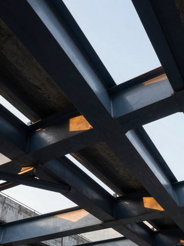 Low-angle architectural shot of massive steel beams and structural concrete under sharp daylight, deep navy shadows and warm golden reflections, professional industrial photography