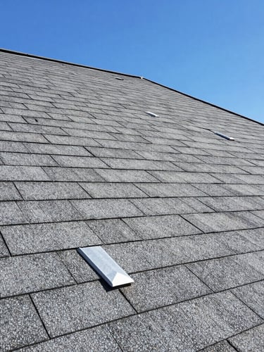Detail shot of clean, newly installed grey architectural shingles and pristine metal flashing on a modern roof, bright clear daylight, sharp focus.