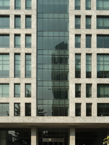 Wide architectural elevation of a modern concrete and glass corporate headquarters in Gurgaon, harsh sunlight casting sharp geometric shadows, desaturated green accents, 24mm