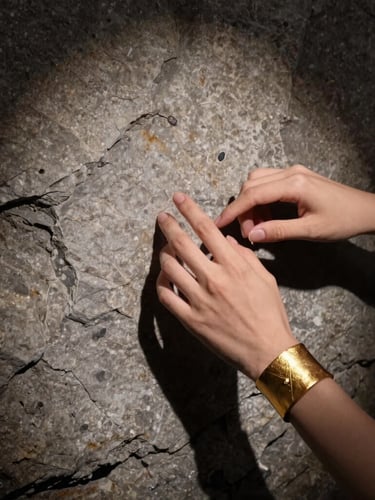 Fine art jewelry photography of hands with expressive gestures interacting with a heavy gold textured cuff, raw stone background, dramatic side spotlight, Hasselblad 80mm