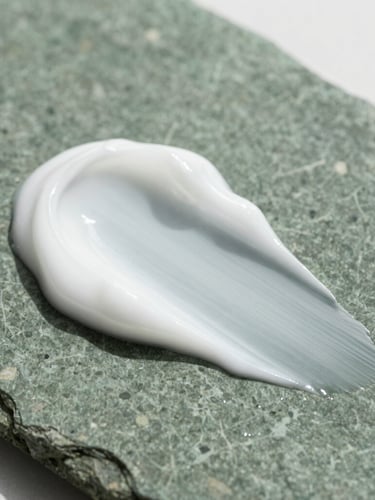 Macro editorial photograph of smooth white toothpaste paste texture on a dark green stone surface, soft natural daylight, high-end wellness aesthetic