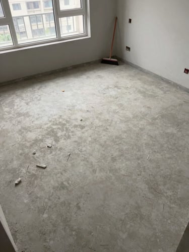 Close overhead view of a completely empty swept concrete floor in a cleared apartment, natural north-facing daylight through bare windows, a single broom resting against the wall, no clutter — documentary stillness after clearance work