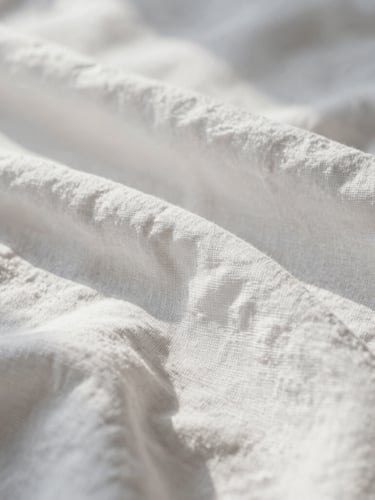 Tactile close-up of perfectly pressed, high-thread-count white linen, soft morning light casting gentle shadows, elegant composition.
