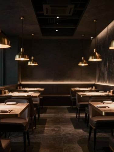 Wide shot of an empty, sleek, modern Asian fusion restaurant dining room, low hanging pendant lights casting warm glow, dark charcoal walls, brass accents, high-contrast, dramatic side-lighting, shallow depth of field