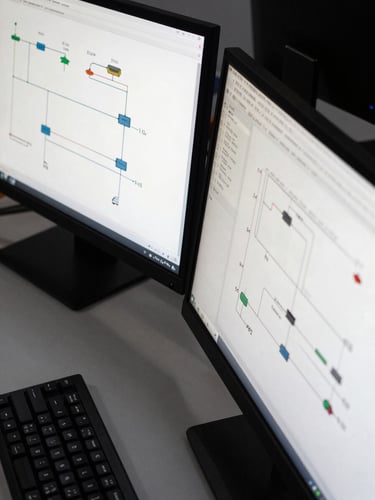 Close-up overhead view of an engineering workstation: two monitors displaying system architecture diagrams with connector lines and module labels, a mechanical keyboard partially visible, flat cool office daylight from above, no people, sharp technical detail
