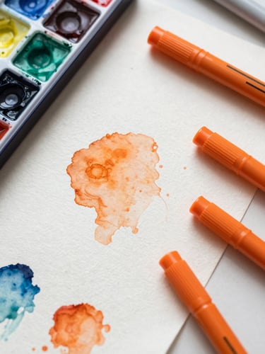 Overhead flat-lay macro photography of a messy, pigment-stained studio desk, watercolor washes, vibrant orange alcohol markers, textured paper, soft natural daylight, 50mm lens.