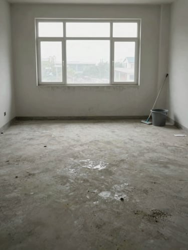 Wide shot of a freshly cleared room interior, bare concrete floor recently swept, a mop and bucket in the far right corner, overcast daylight through a large window, no furniture, documentary framing