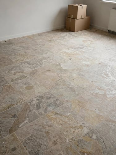 Overhead wide shot of a cleared apartment floor after débarras, stone tile visible, a few remaining cardboard boxes stacked near the far wall, overcast natural light, documentary style, no people