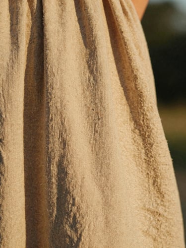 Close-up of textured linen fabric being held, warm golden-hour sunlight, earthy sand-washed tones, candid lifestyle feel, 35mm film.