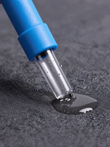 Macro shot of a professional extraction nozzle drawing dirty water from a dark grey fabric, water droplets visible inside the transparent nozzle, bright studio lighting, electric blue accents
