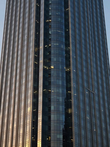 Sharp architectural angle of a modern financial district skyscraper in New Delhi, deep navy glass facade reflecting soft morning window light, professional 50mm corporate photography
