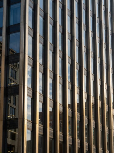 Architectural detail of a modern financial district with high-contrast corporate daylight reflecting off structured glass panels