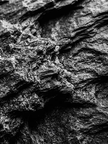 Macro photography of dark slate texture with deep shadows, dramatic side-lighting, high-contrast black and white, tactile organic material, 35mm