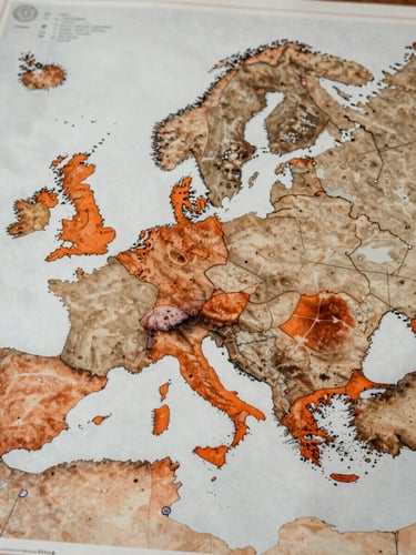 Close overhead wide shot of a European map schematic printed on aged paper, Greece and southern Europe highlighted with a single burnt orange overlay zone, northern EU routes marked with thin lines, overcast diffused light, no text or labels, documentary industrial feel
