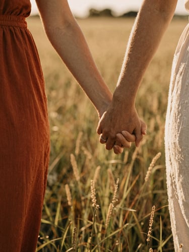Close-up of a couple's hands gently clasped while walking through a sun-drenched field of wild grass, warm golden hour light, shallow depth of field, 35mm film look