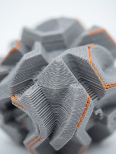 Prim-plan macro cu un obiect printat 3D cu textură fină, evidențiind straturile perfecte, lumină de studio curată, accente subtile portocalii.