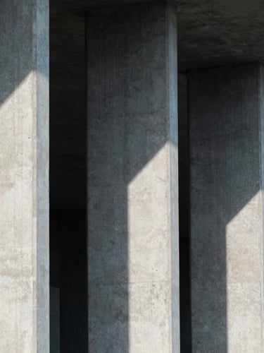 A close-up architectural shot of concrete pillars and sharp geometric shadows under cool, diffused daylight, emphasizing structural integrity.