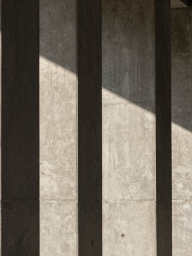 A vertical architectural crop of concrete columns casting sharp geometric shadows under diffused daylight.