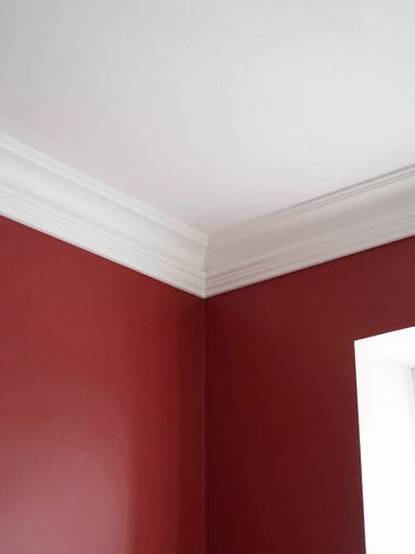 Clean architectural photography of a finished room interior, crisp white crown molding against deep red walls, bright natural daylight, sharp focus, 35mm