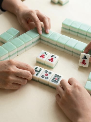 Overhead flatlay of hands arranging physical Mah Jongg tiles on a clean ivory table, soft natural window light, warm editorial style.