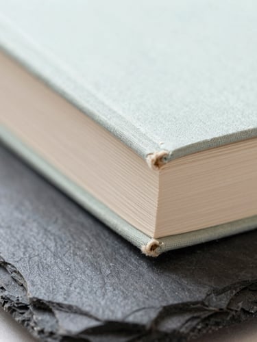 Close-up of a minimalist book spine bound in rough linen, resting on a dark slate surface, soft natural side-light, macro detail.