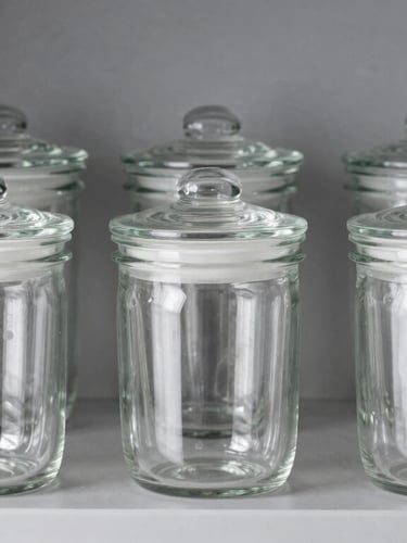 Pristine glass storage jars with airtight lids, arranged neatly on a clean gray shelf, bright studio lighting, crisp reflections