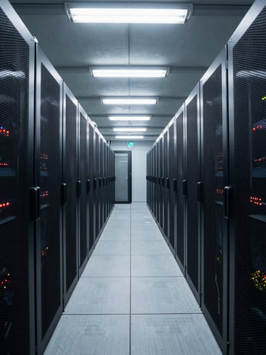 Wide environmental shot looking down a data center corridor, rows of illuminated server racks receding into depth, cool clinical overhead fluorescent lighting, no people, shot from a low centered angle with strong linear perspective