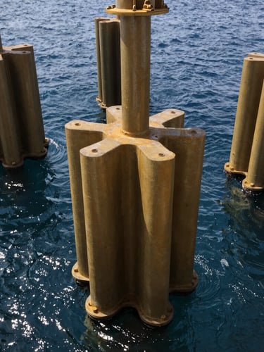 Close-up of industrial marine engineering equipment, heavy steel piles being positioned in deep navy water, bright daylight, sharp focus