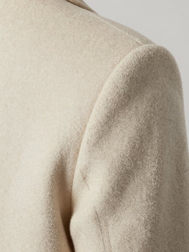 Extreme close-up of a tailored cream-colored wool coat shoulder seam, soft diffused studio lighting, high-contrast neutral tones, macro texture detail.