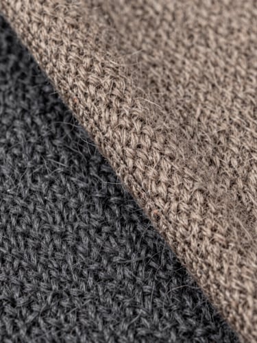 Macro detail of a hand-finished double-faced wool seam, soft diffused studio lighting, displaying the intricate weave of charcoal and warm taupe fibers