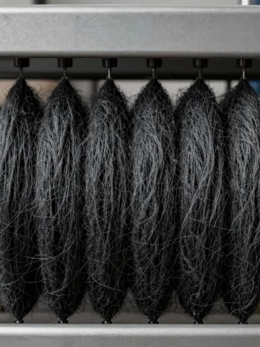 Symmetrical composition of raw charcoal wool fibers being spun on modern, clean industrial machinery, soft lighting highlighting the texture of the charcoal wool thread.