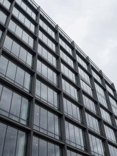 Wide architectural shot of a modern glass office building facade in Warsaw under an overcast sky, clean technical lines, geometric steel structures.